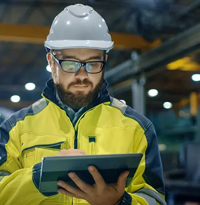 Ein Ingenieur mit Helm arbeitet auf einem Tablet in einer Werkhalle