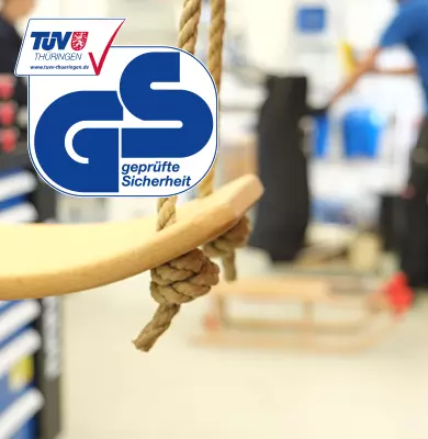 Schaukel mit GS-Zeichen vom TÜV Thüringen, im Hintergrund ein Prüflabor mit Rodelschlitten